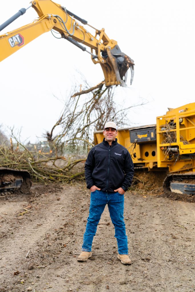 Anthony Nonini standing in front of a CAT excavator and Tigercat grinder during an orchard removal