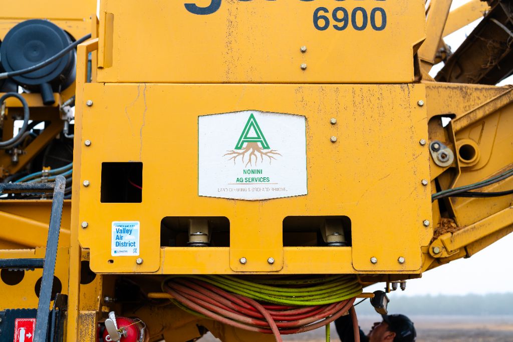 Nonini Ag Services logo sticker and Valley Air District compliance sticker on a Tigercat 6900 grinder at a Central Valley orchard removal job